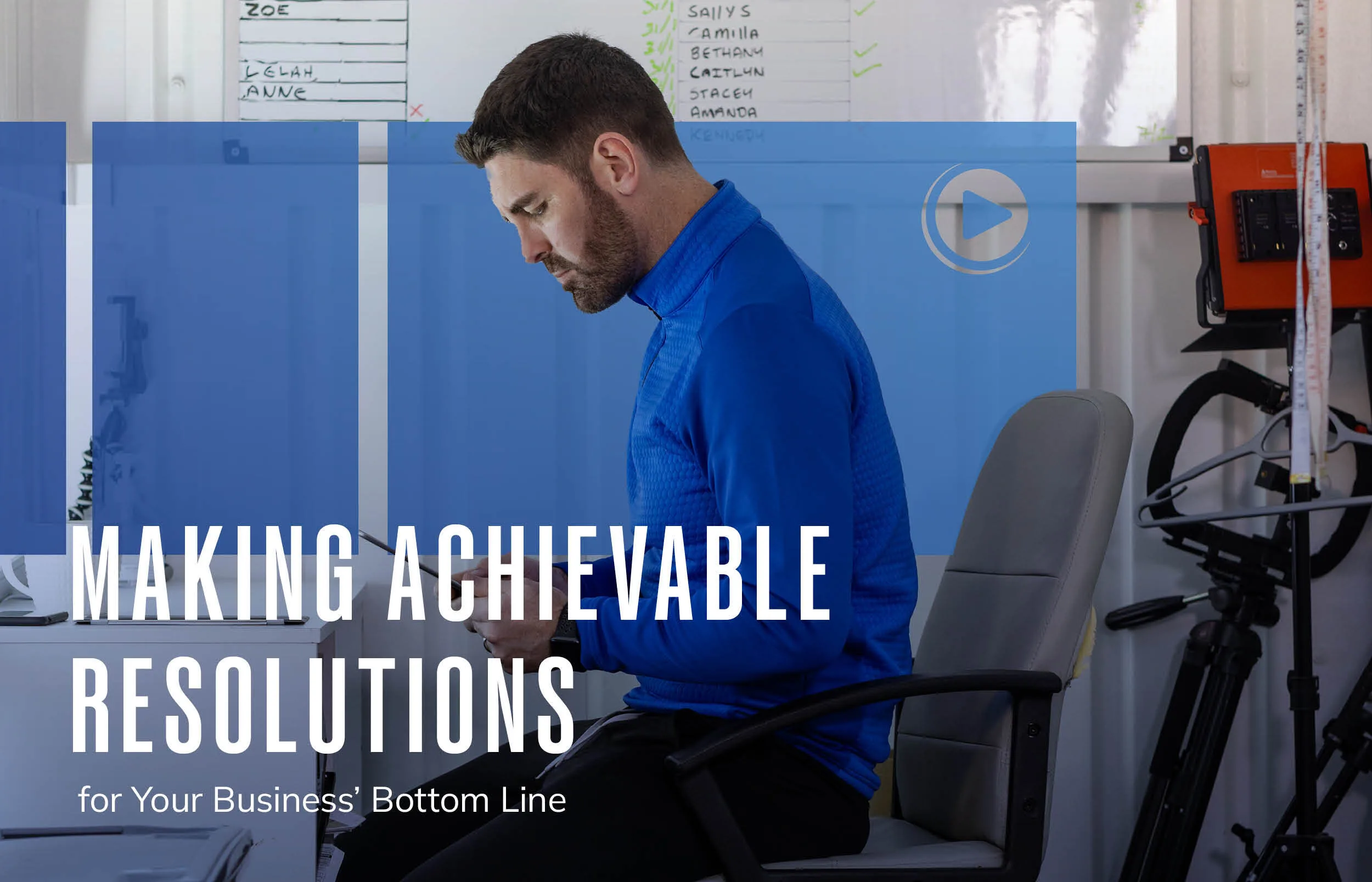 A man sits at a desk reading documents in a workspace with whiteboards behind him. Text overlay reads, “Making Achievable Resolutions for Your Business Bottom Line.”.