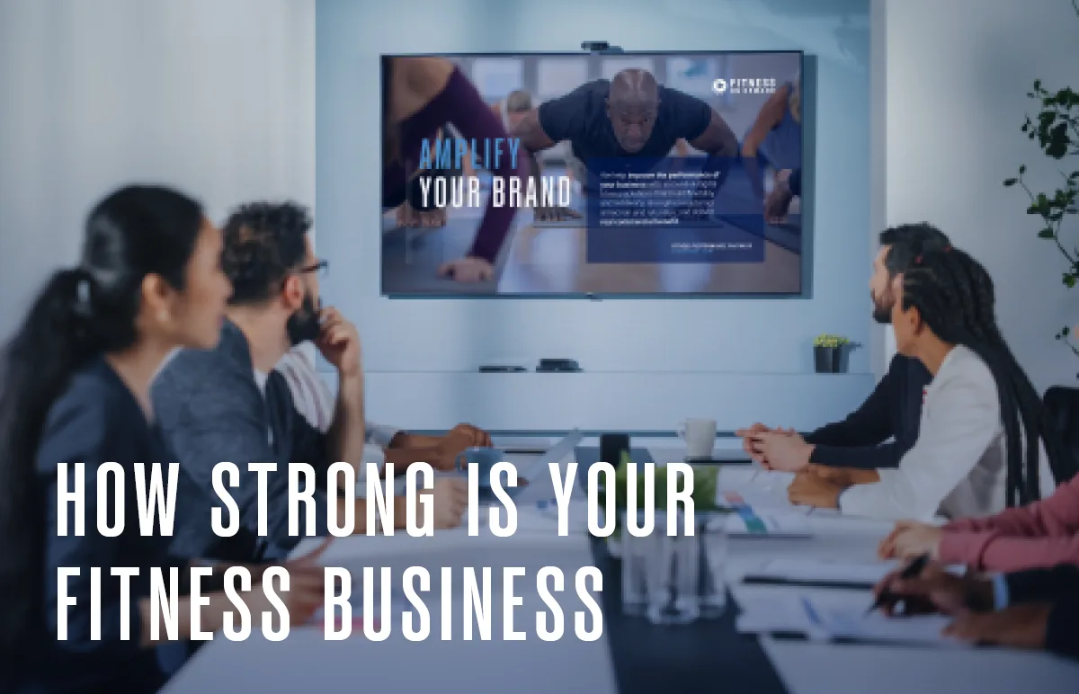 A group of people in a conference room watch a presentation on a wall screen about amplifying a fitness brand, with the text “How Strong Is Your Fitness Business” overlaid in the foreground.