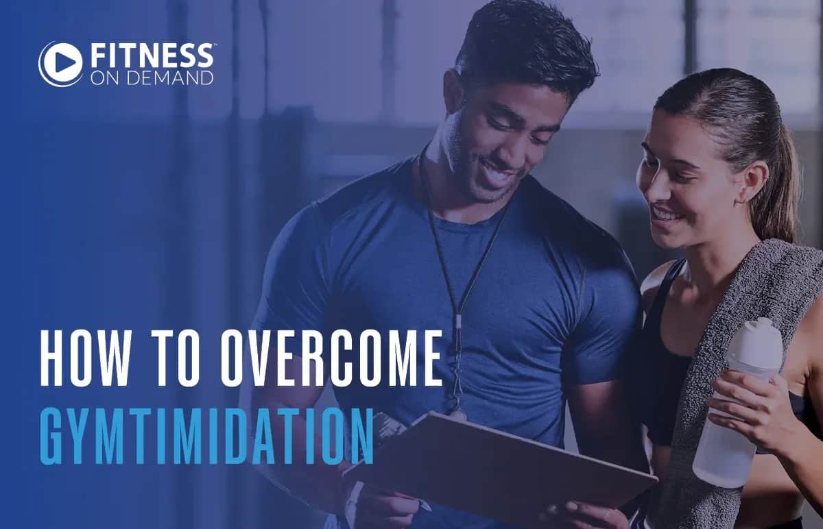 A man holding a clipboard and a woman with a towel and water bottle smile together in a gym. Text reads Fitness On Demand. How to overcome gymtimidation.