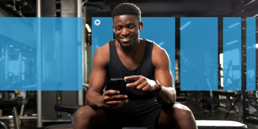 A man in workout clothes sits on a gym bench, smiling while looking at his smartphone. He appears relaxed, with exercise equipment visible in the background. Blue translucent rectangles overlay the image.